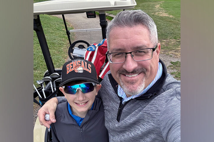 A preteen boy stands with his father in front of a golf cart