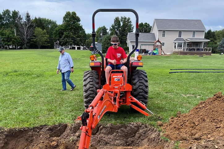 A preteen boy helping his father use a backhoe