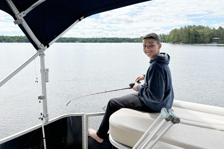 An 11-year-old boy smiles while fishing with crutches propped up next to him.