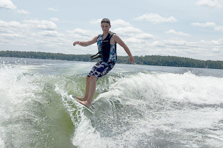An 11-year-old boy surfs the top of a wake on a lake.