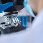 A person wearing latex gloves looks at a microscope