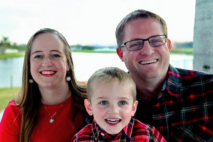 A smiling woman and man with a happy young boy in front of a body of water.