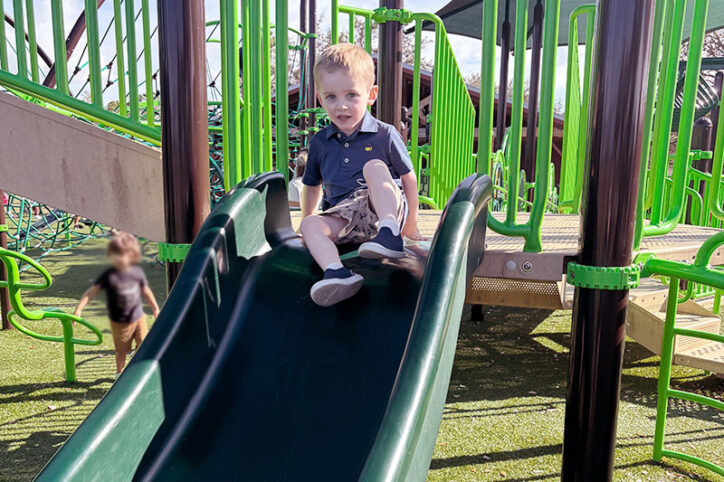 A young boy gets ready to go down a slide on a jungle gym.