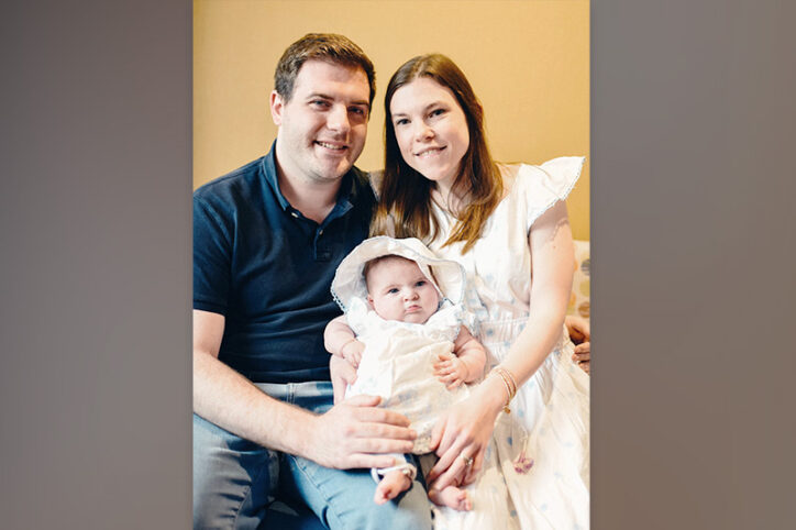 A father and mother seat their infant daughter on both of their laps.