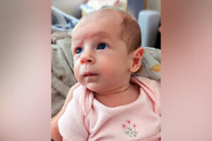 A baby gazing up and to the left while lying on a dinosaur-patterned blanket.