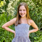 a smiling preteen girl with her hands on her hips