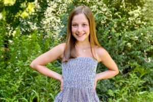 a smiling preteen girl with her hands on her hips