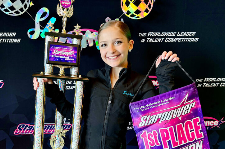 A smiling preteen girl holding a sign and first place trophy 