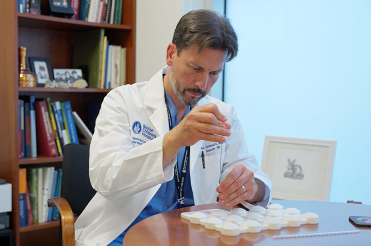 A man in a white lab coat sitting at a table dropping liquid into a tray case.
