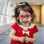 A young girl with a tracheostomy smiles while standing in a hospital hallway.
