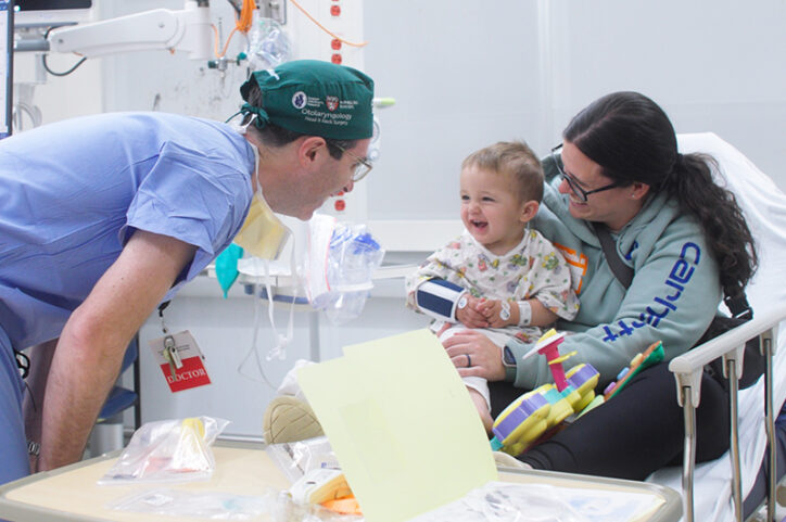 A doctor makes a toddler laugh while his mother holds him in a hospital bed.