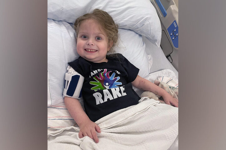 A smiling young girl in a hospital bed with a t-shirt that says, "rare."