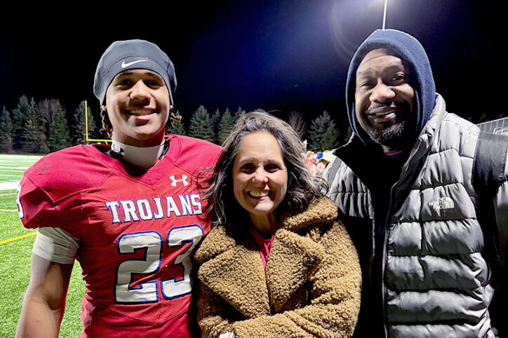 A teen boy standing on a football field with his mother and father