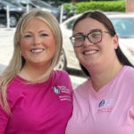 Two young women wearing pink shirts, standing together and smiling.