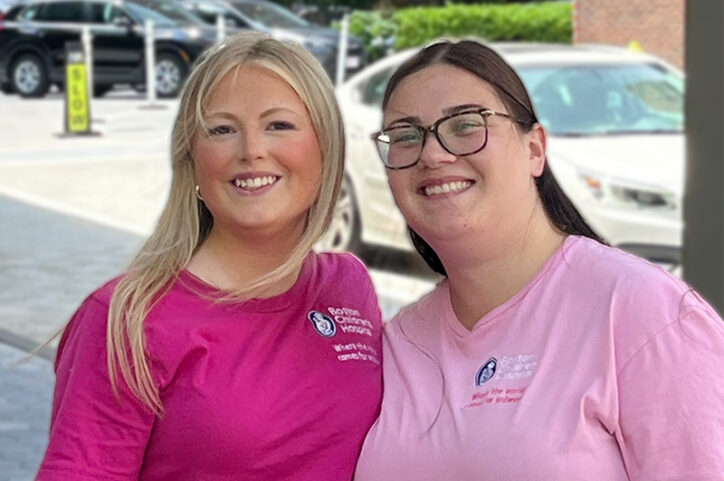 Two young women wearing pink shirts, standing together and smiling.