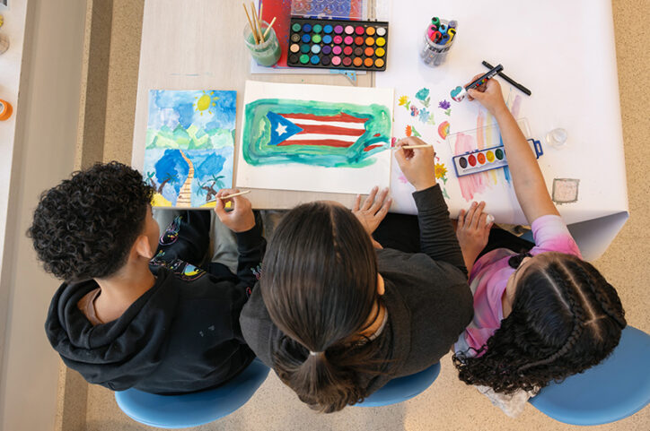 An overhead view of a woman and two children creating watercolor paintings at a table.
