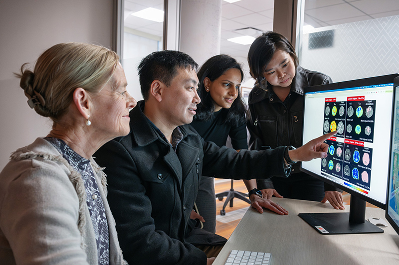Four clinicians reviewing neonatal brain imaging on a computer in an office.