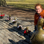 a young adult poses by the Make Way for Ducklings statues on Boston Common