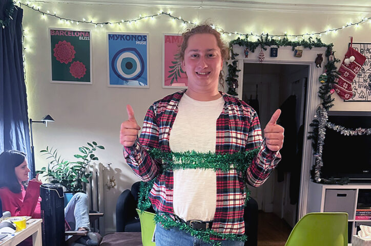 A smiling young adult wrapped in Christmas tinsel gives two thumbs up