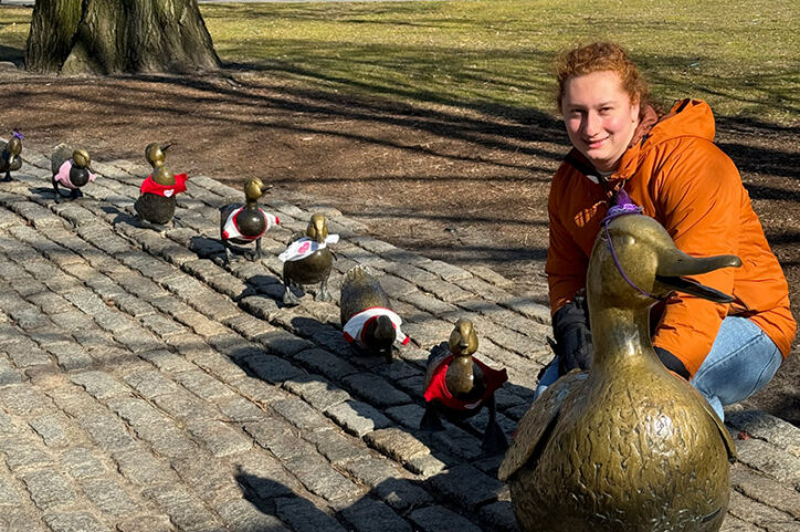 a young adult poses by the Make Way for Ducklings statues on Boston Common