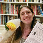 a smiling female young adult holds a bouquet of flowers and a certificate showing she won the Moth Story Slam
