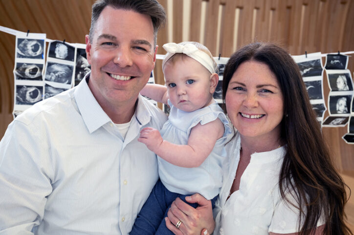 A man and woman holding a baby in a headband, smiling at the camera.