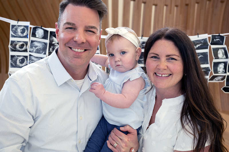 A man and woman holding a baby in a headband, smiling at the camera.