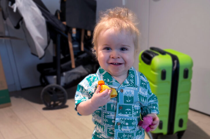 A young boy holds toys in both hands and offers a wide smile.