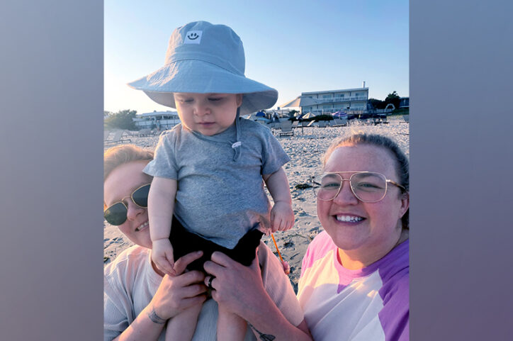 Two women lift a young boy on a beach.