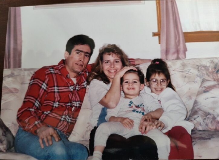 Grainy photo of a man, woman, young boy, and young girl smiling together while sitting on a couch.