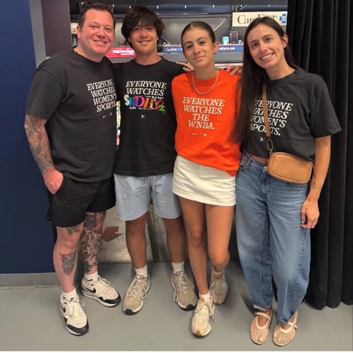 A man, teen boy, girl, and woman smile together wearing 'Everyone Watches Women's Sports' t-shirts at an arena.