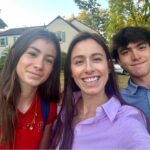 A woman smiles in an outdoor selfie with a teenage boy and girl.