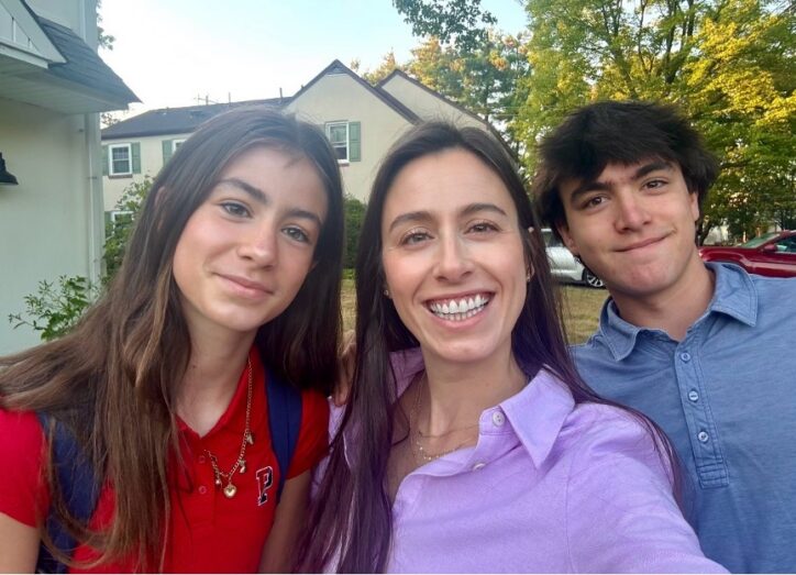 A woman smiles in an outdoor selfie with a teenage boy and girl.