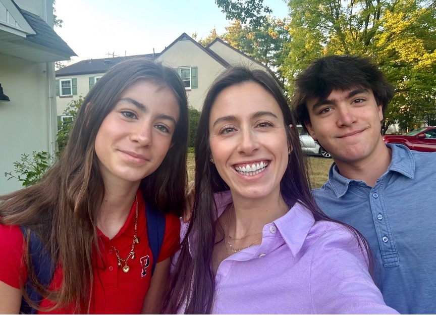 A woman smiles in an outdoor selfie with a teenage boy and girl.