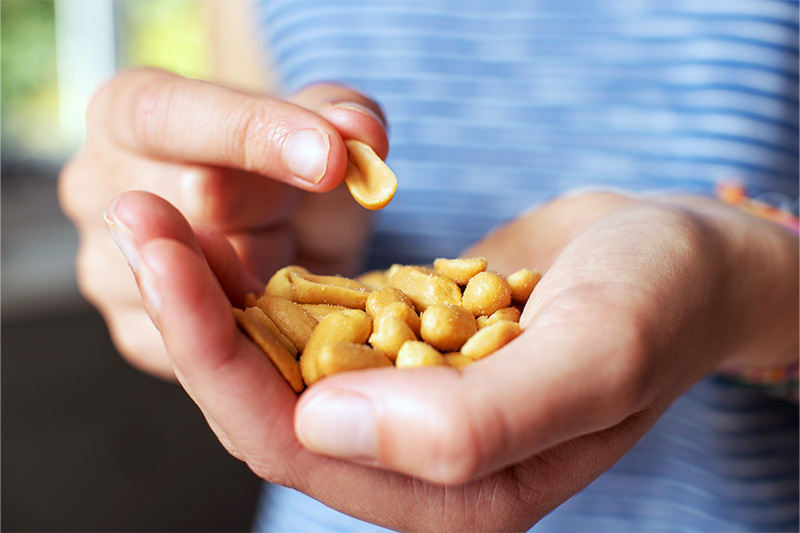 A person holds a handful of peanuts while picking one up with the other hand.