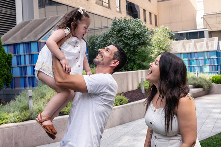 A man lifts his young daughter into the air while her mother looks on