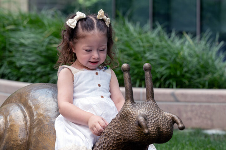 a young girl sitting on a snail sculpture in Boston Children's rooftop garden