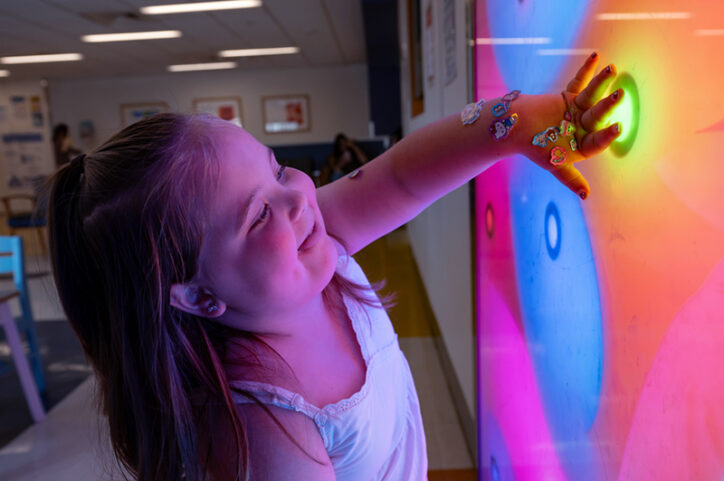 A young girl pressing her hand against a color-changing wall in a hospital waiting room