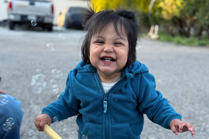 A toddler in a blue hoodie laughing while playing with bubbles.
