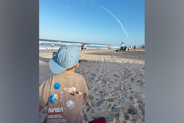 A young boy on a beach watches the launch of the Artemis II mission spacecraft.
